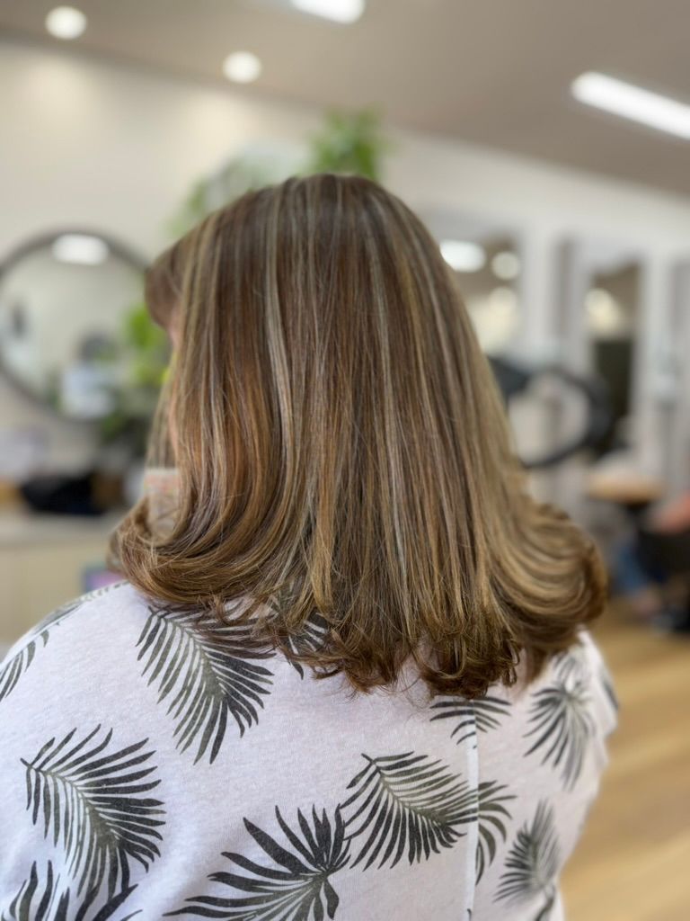 Back view of shoulder-length highlighted hair in a bright salon with mirrors and styling chairs