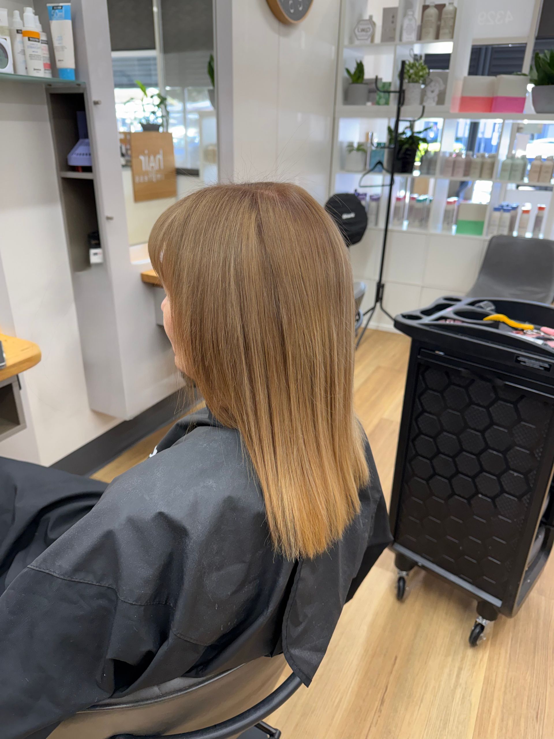 Person with long braided hair seated in a salon chair, facing a mirror with hair tools nearby.