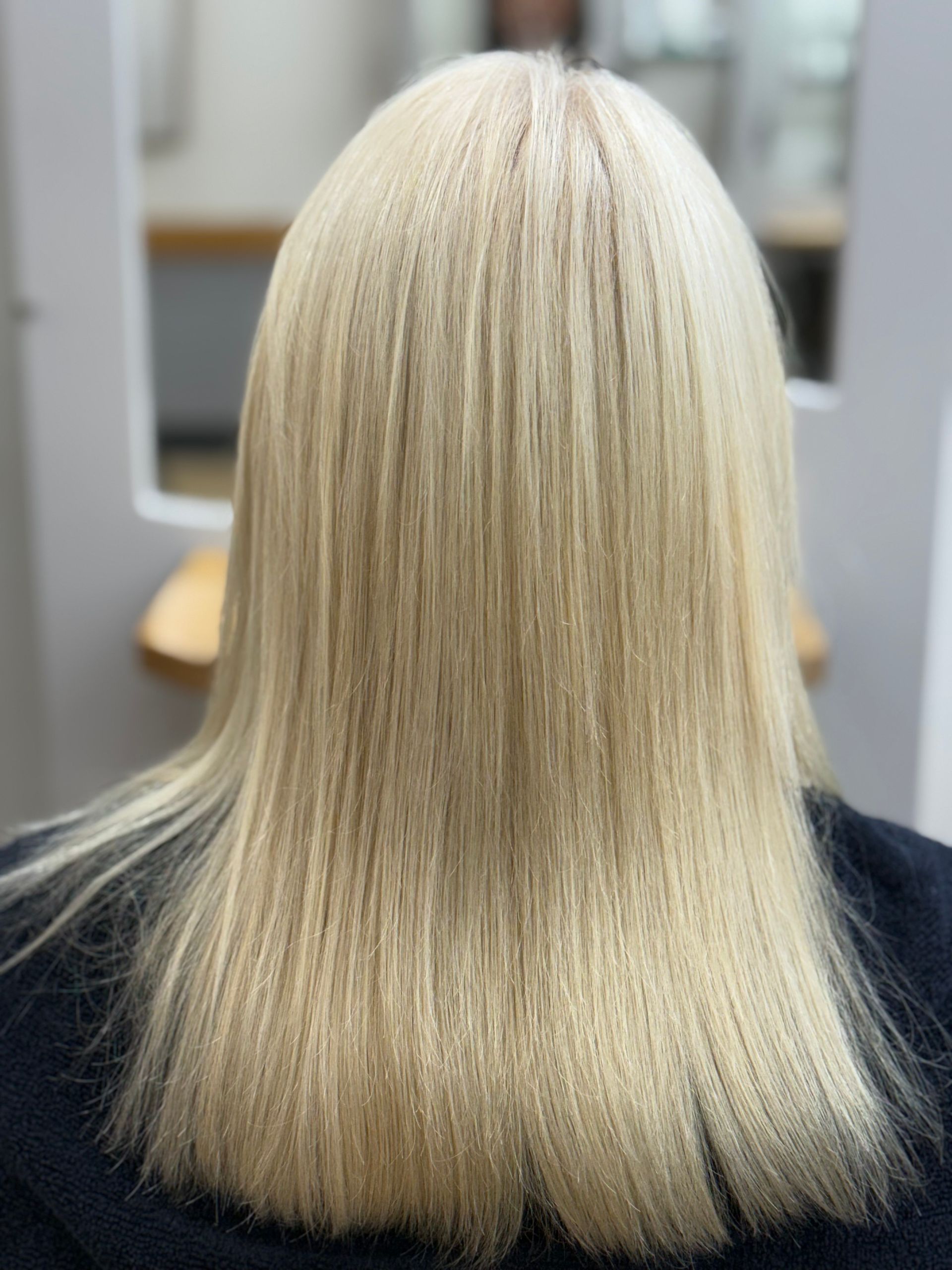 Back view of straight, shoulder-length platinum blonde hair in a salon chair