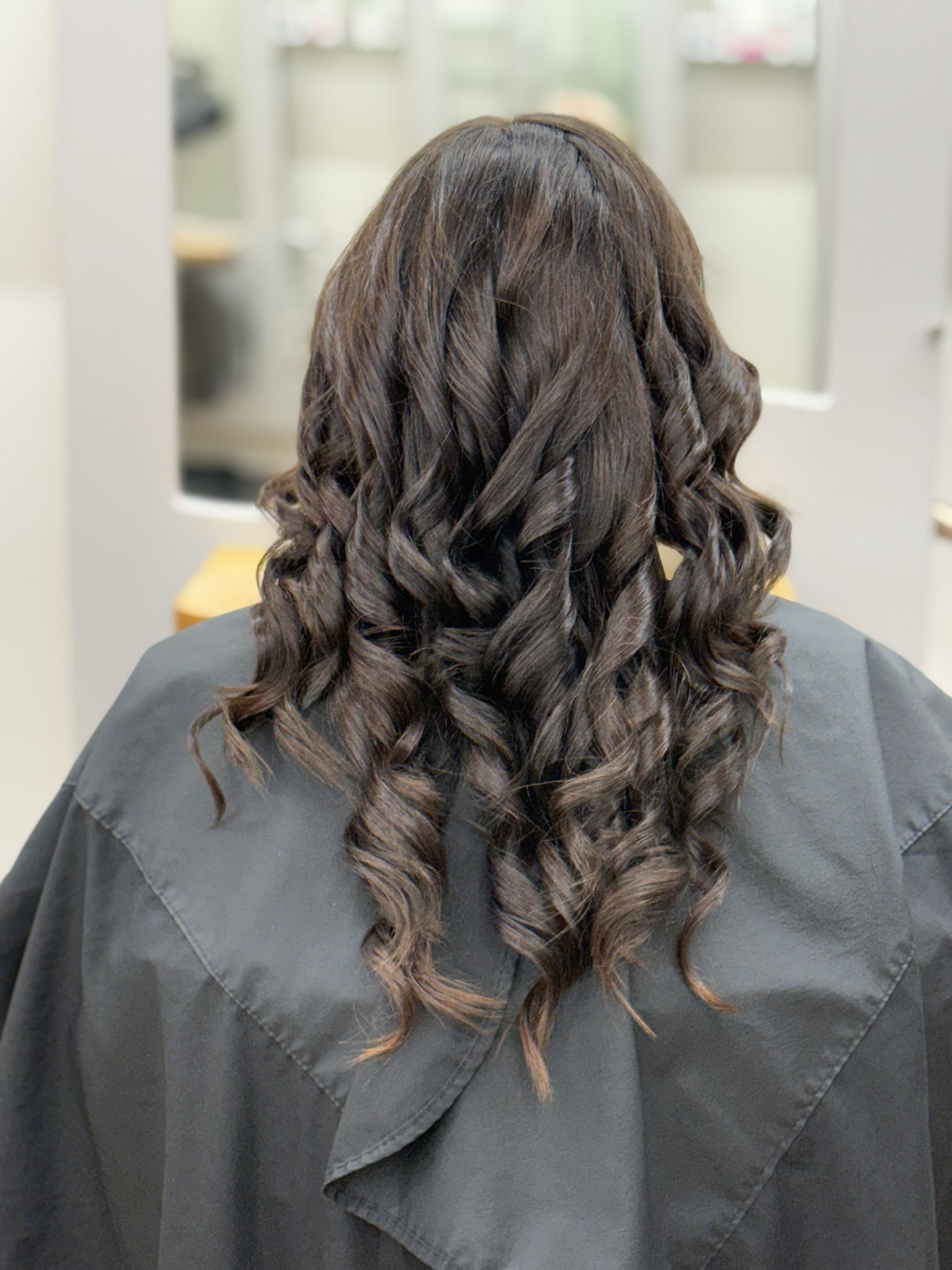 Wavy dark hair styled in loose curls, seen from behind in a salon chair