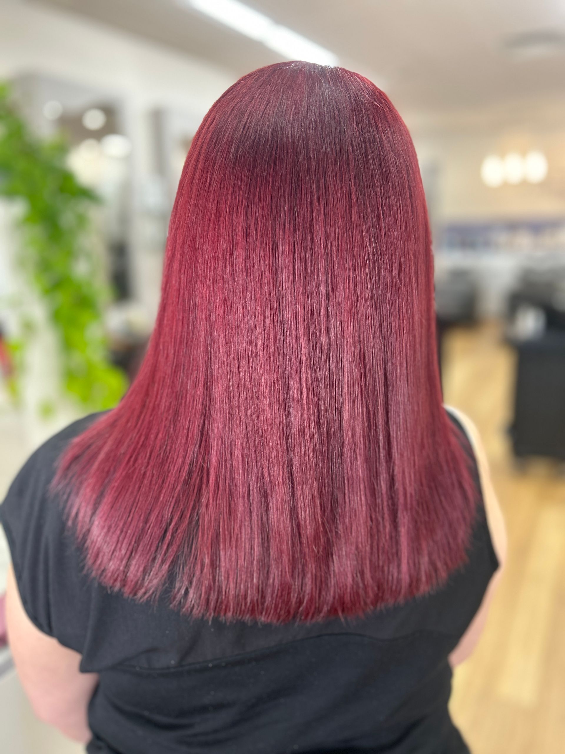 Person with straight burgundy hair seen from behind in a salon interior