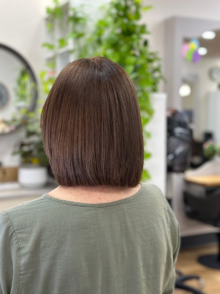 Back view of a person with a short brown bob haircut in a salon with mirrors and plants