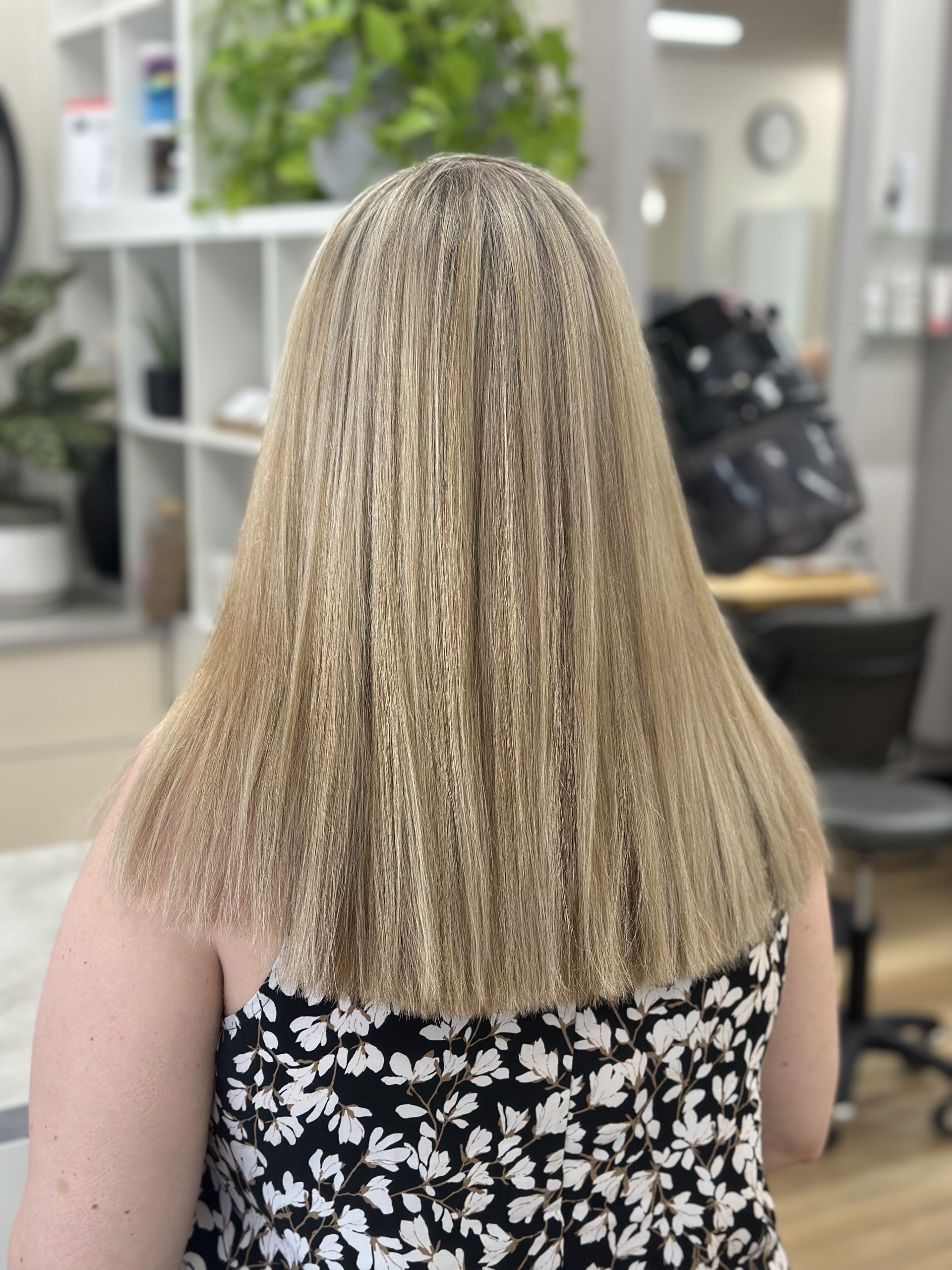 Back view of a person with long blonde hair in a floral dress sitting in a salon chair