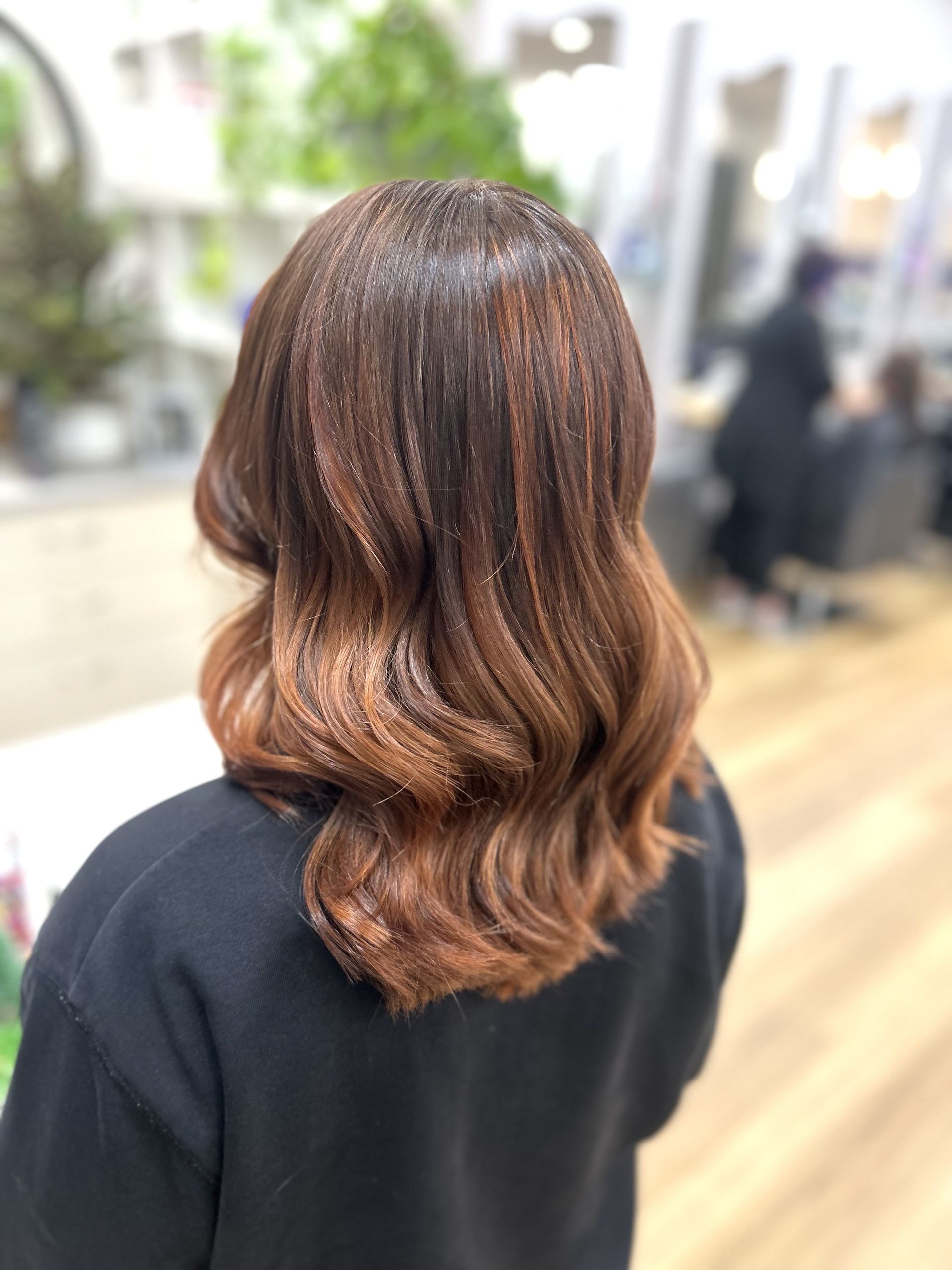 Back view of shoulder-length wavy brown hair with copper highlights in a salon setting