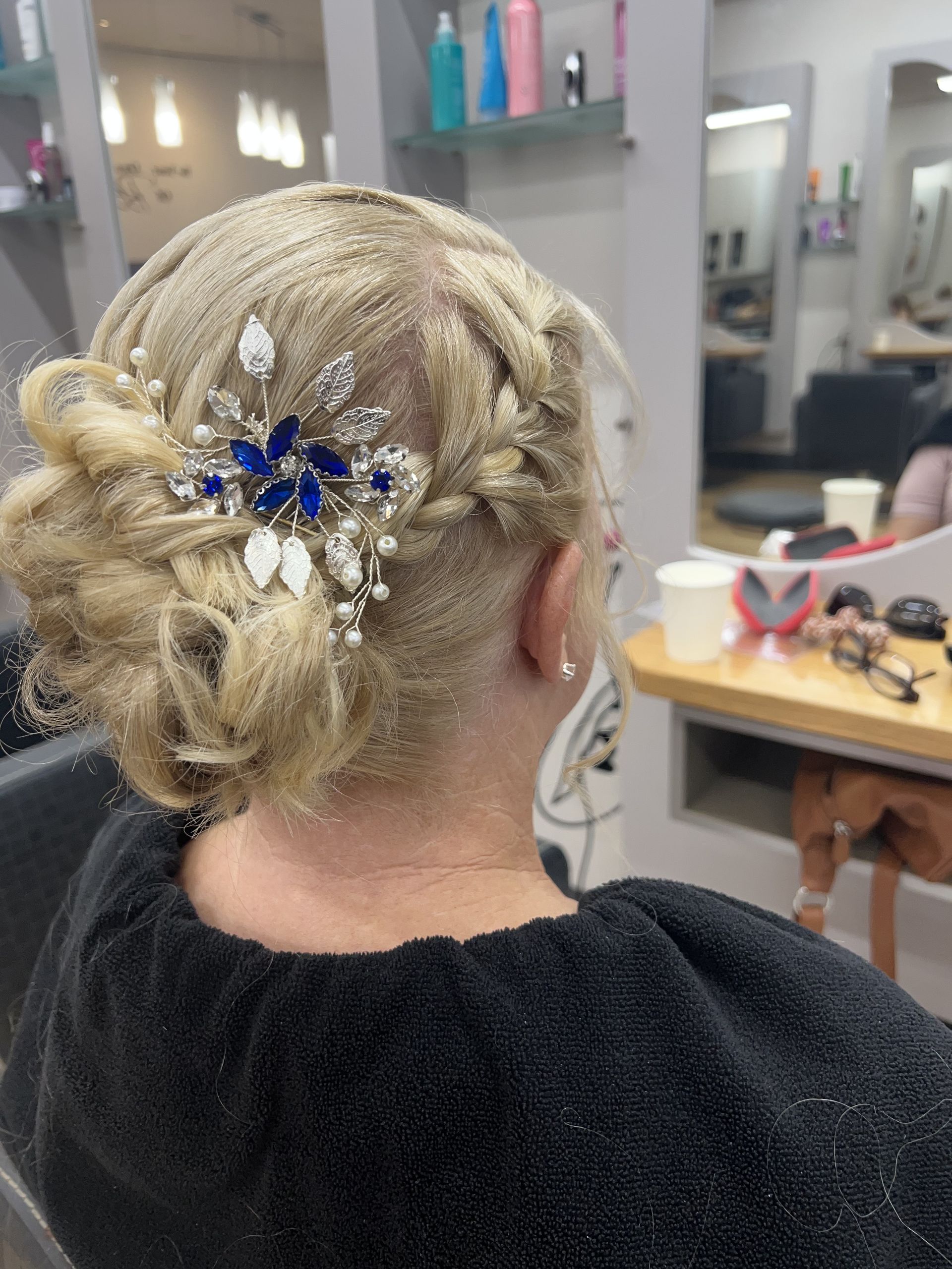Blonde braided updo with a blue floral hair accessory in a salon setting