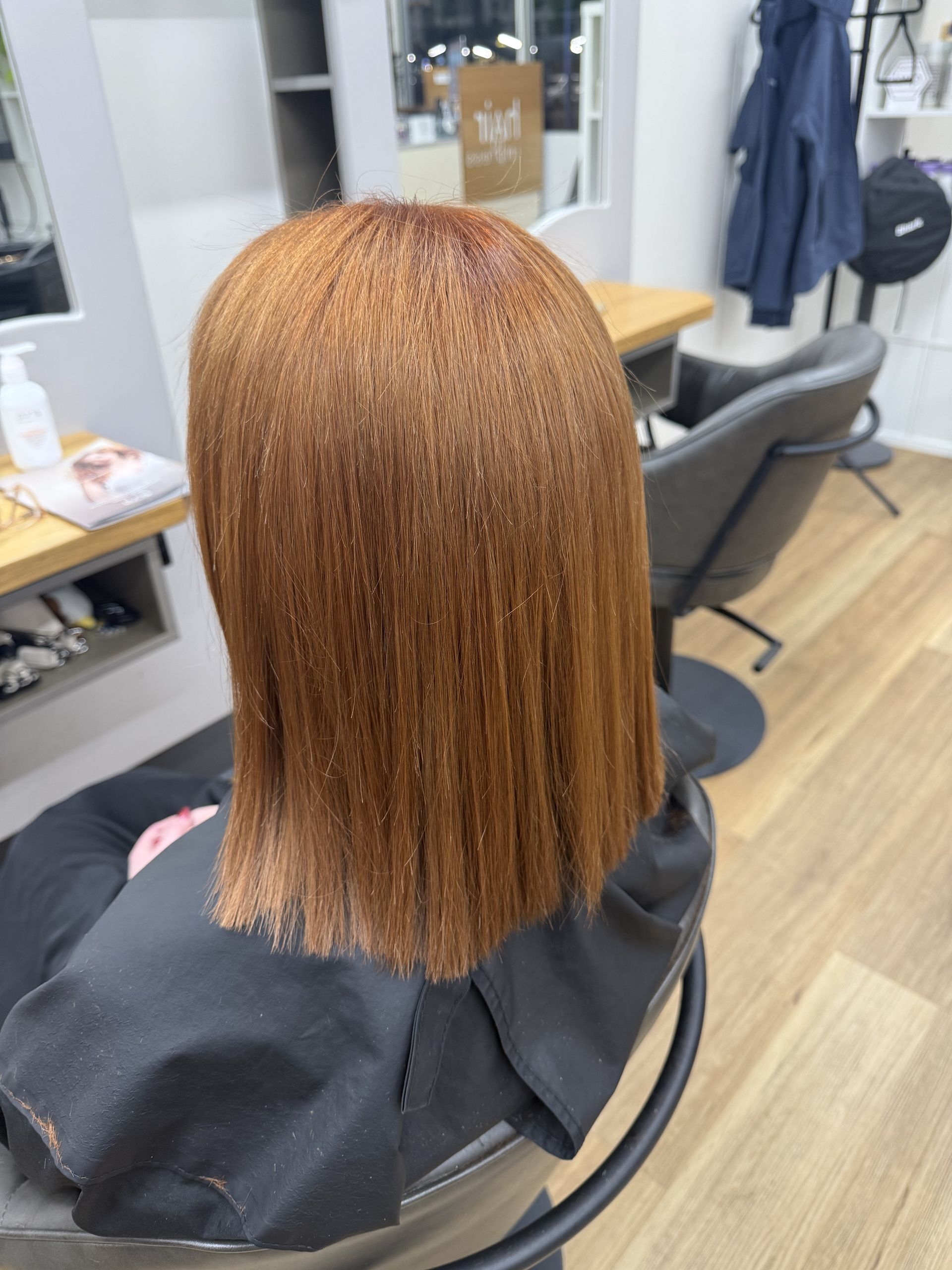 Straight copper-colored bob haircut viewed from behind in a salon chair