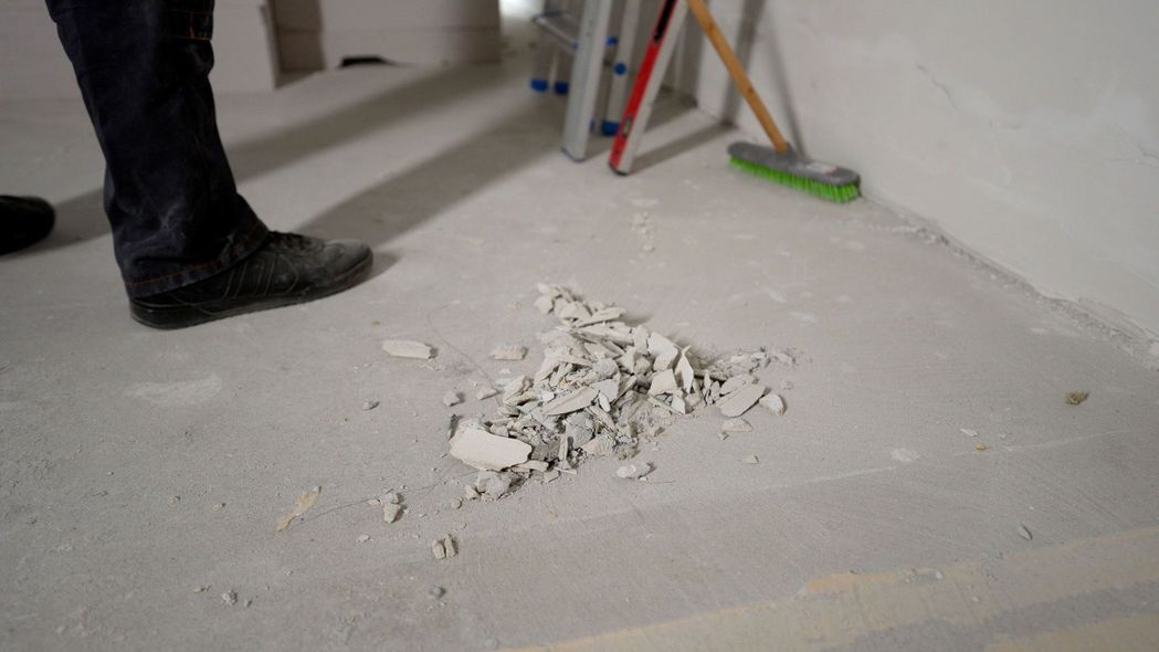 Person's feet near debris on a concrete floor in a room under construction.