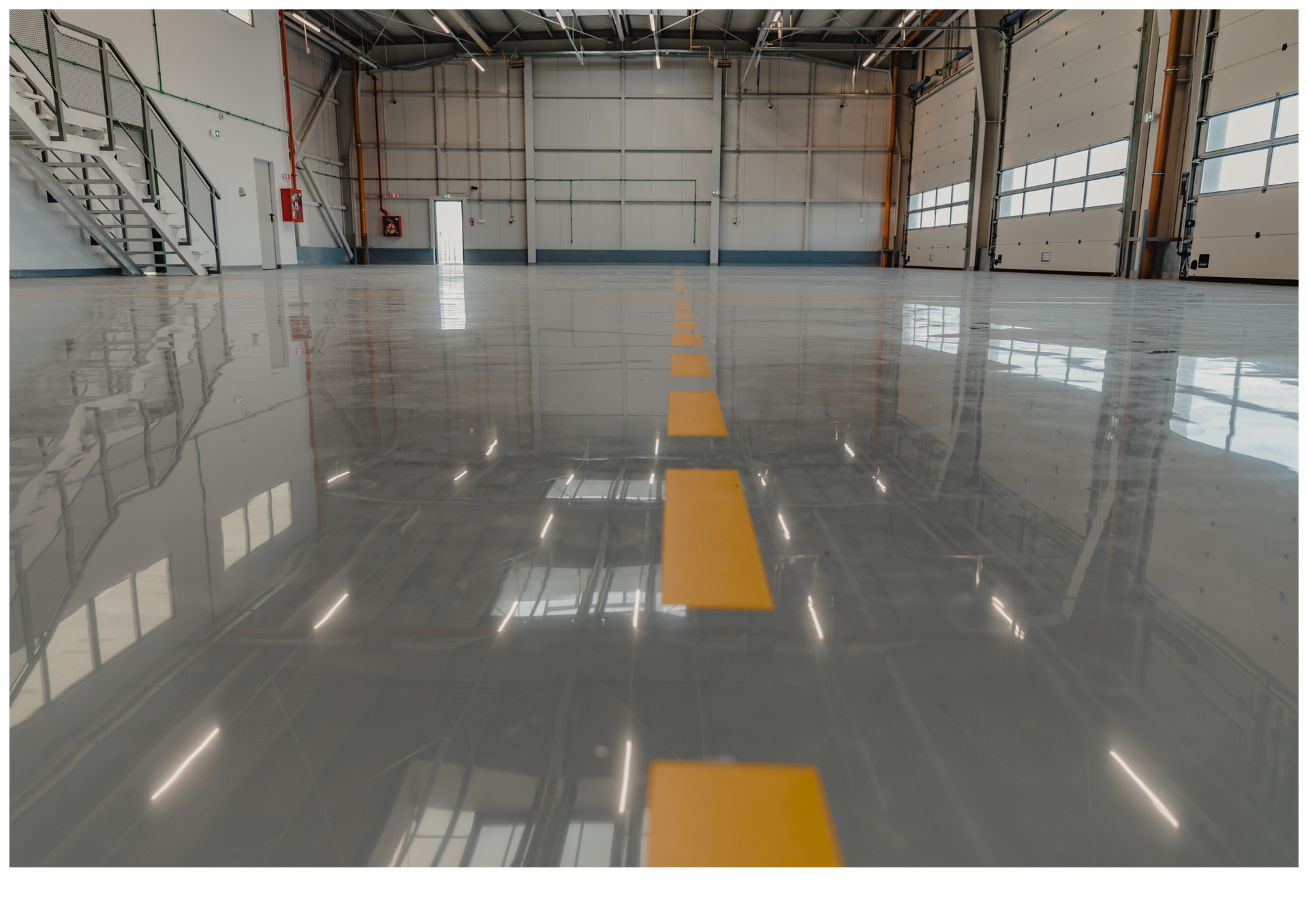 Empty hangar with a glossy floor and a yellow center line leading to a closed white door.