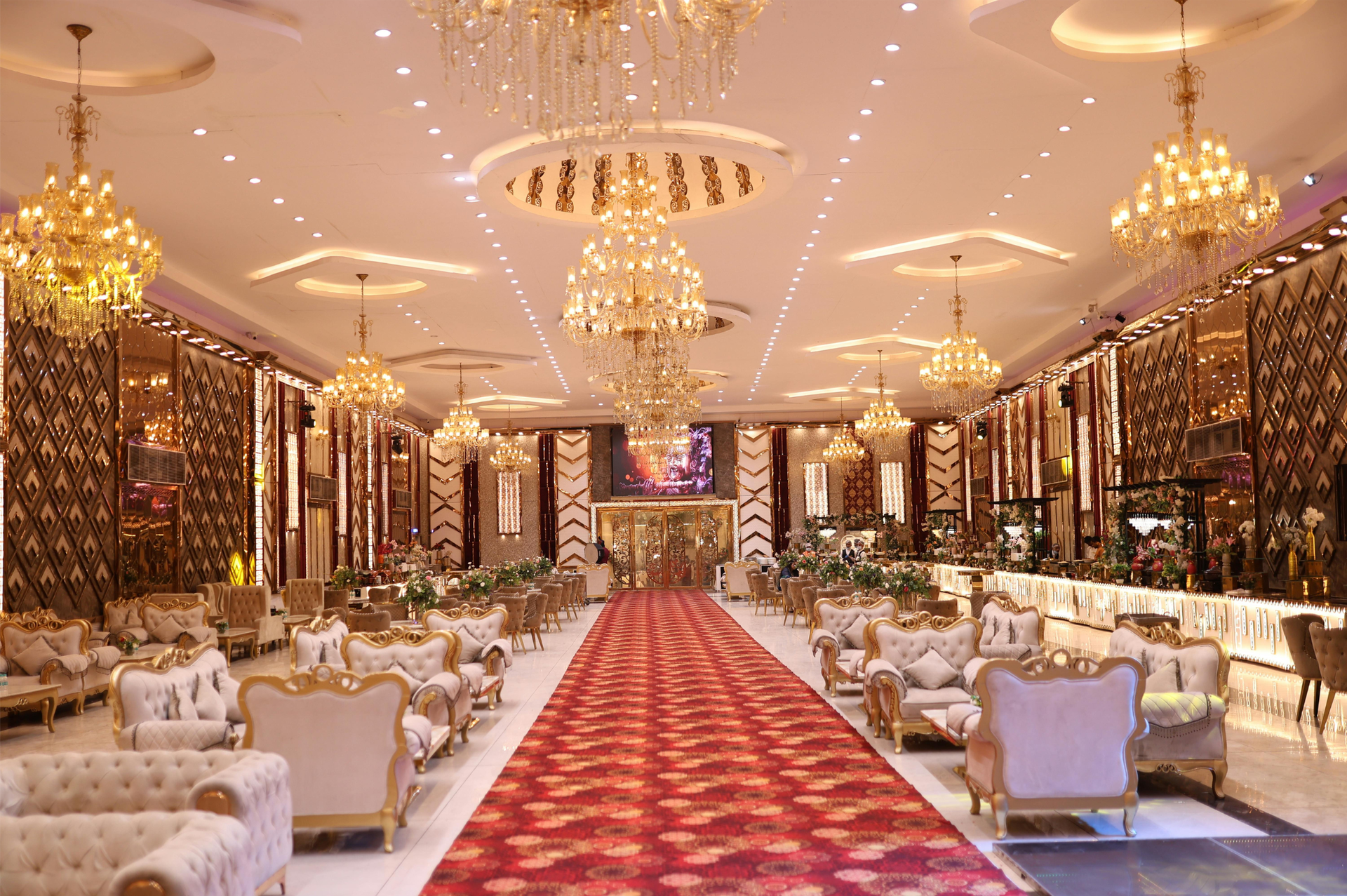 Elegant banquet hall with chandeliers, red carpet aisle, and white tables decorated with floral arrangements
