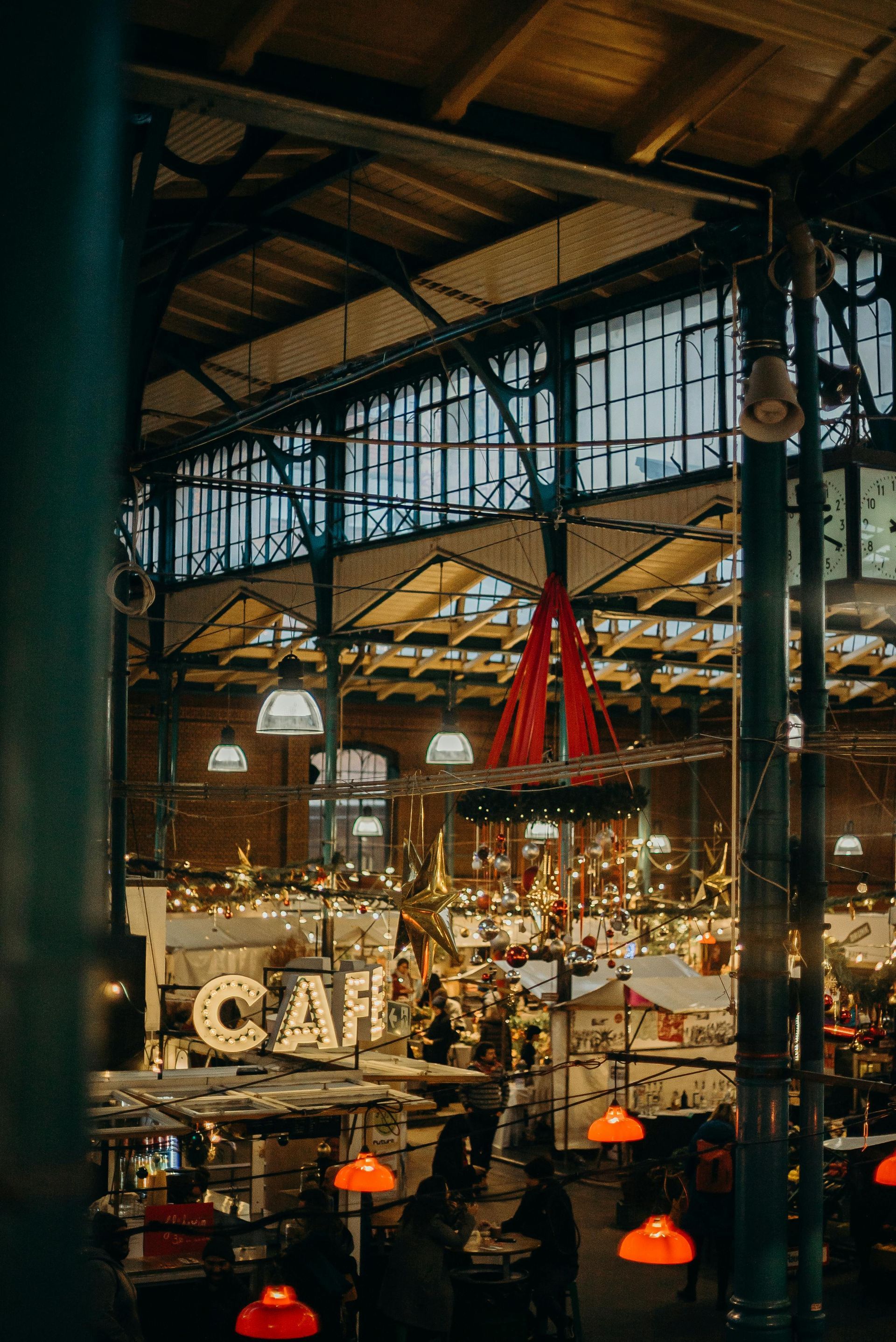Indoor market hall with hanging lights, metal beams, and a red decorative ribbon in a busy dining area