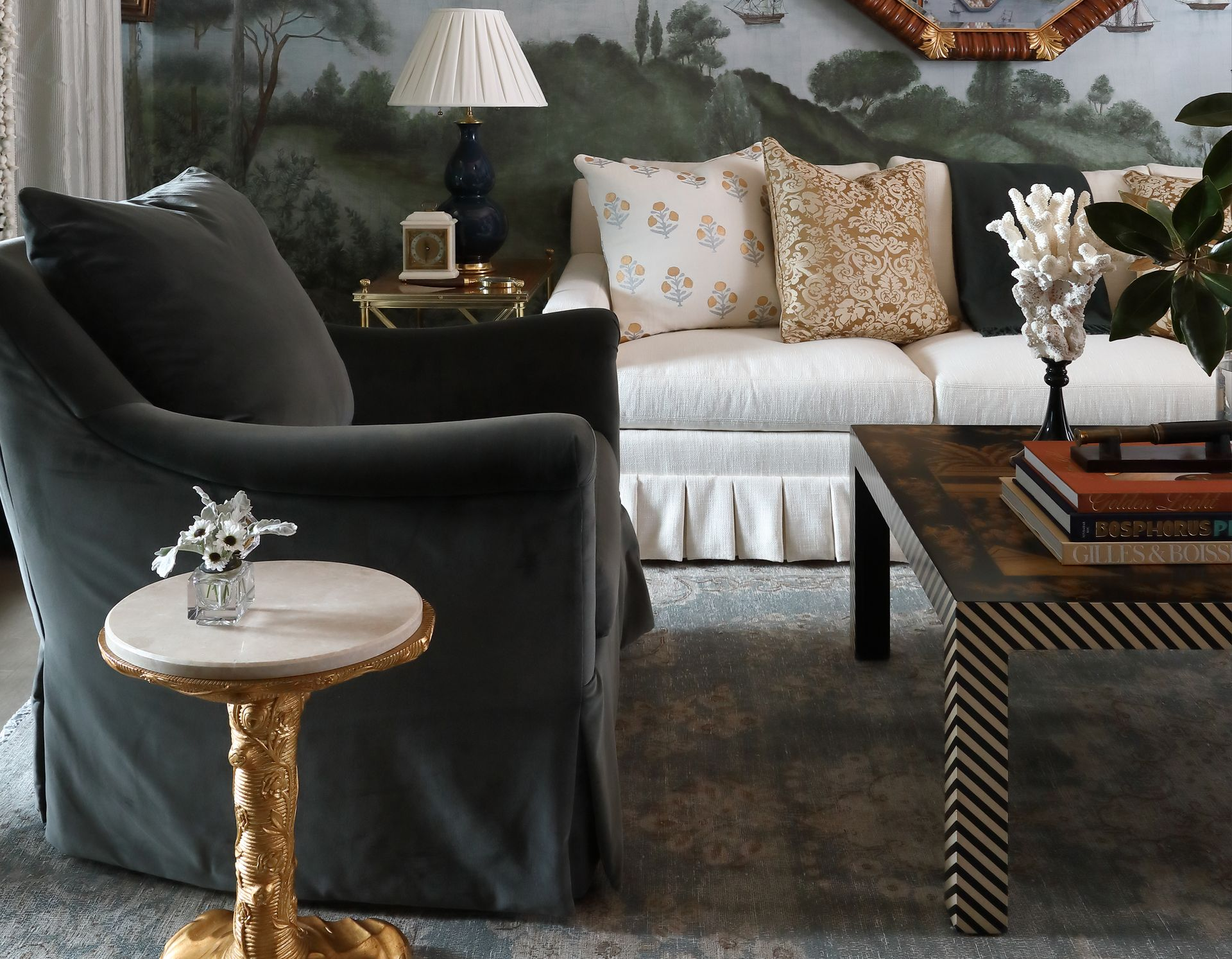 Living room with gray armchair, white sofa, ornate side table, coffee table, and landscape mural.
