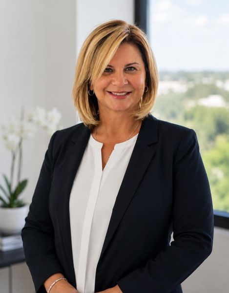 Portrait of a smiling professional in a black blazer and white blouse, standing in an office