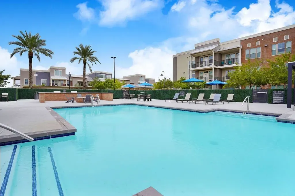 Swimming pool with lounge chairs and umbrellas, apartment buildings in the background.