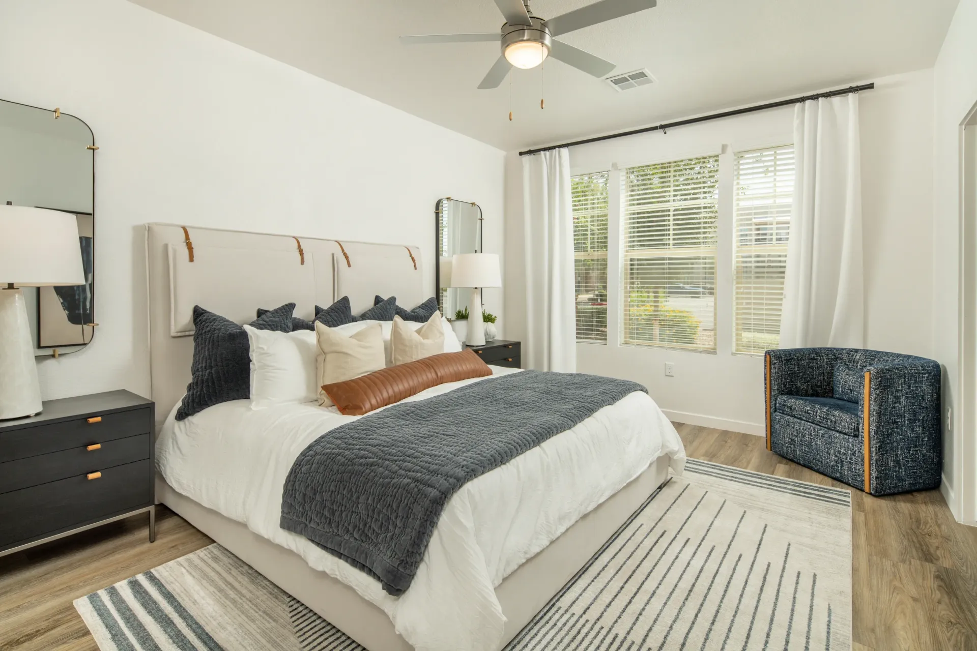 King size bed with navy and beige bedding, and a ceiling fan.