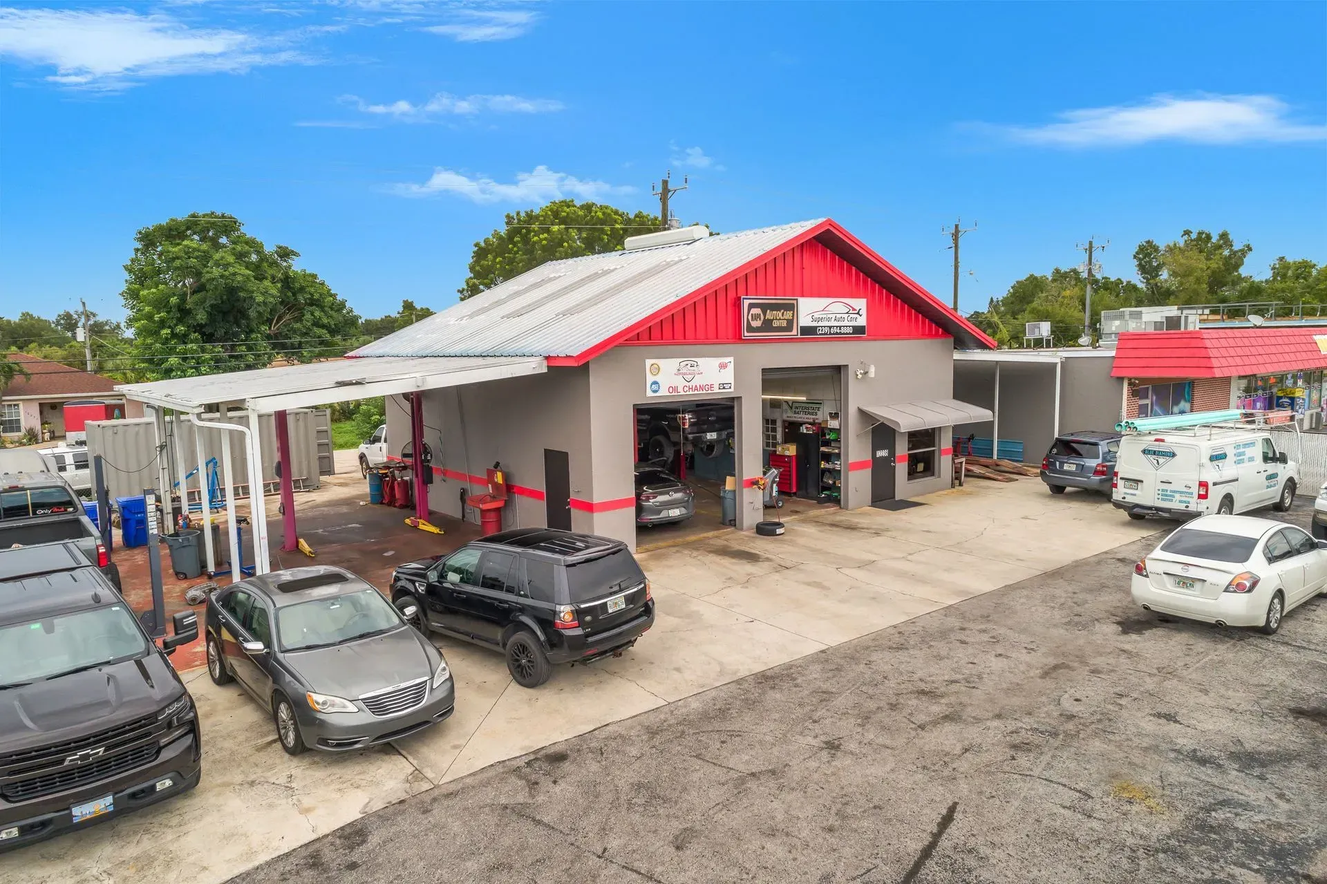 Auto repair shop with red roof and several parked cars on a dirt lot under a blue sky