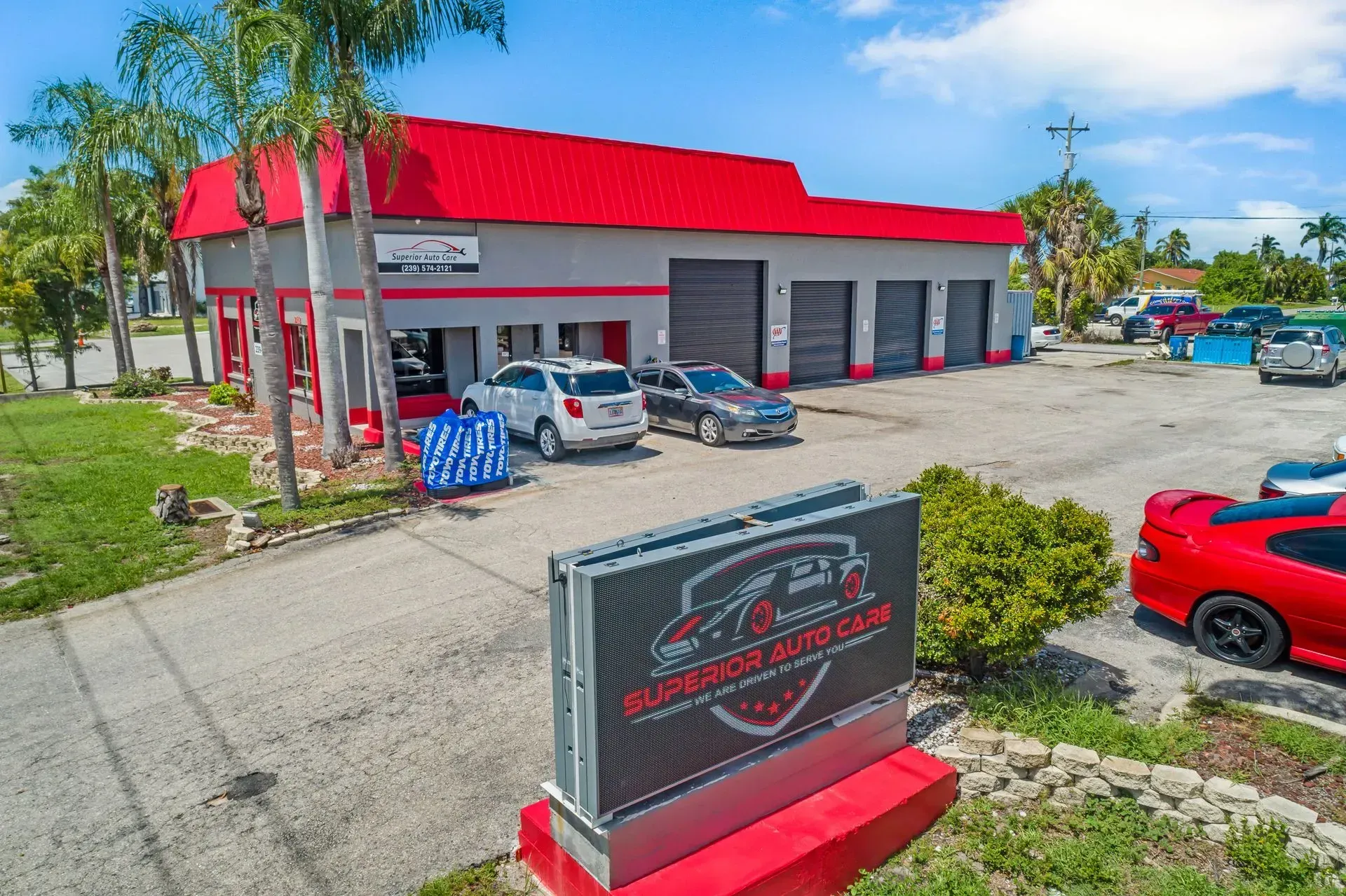 Commercial building with a red roof, parked cars, and a sign in front under a blue sky