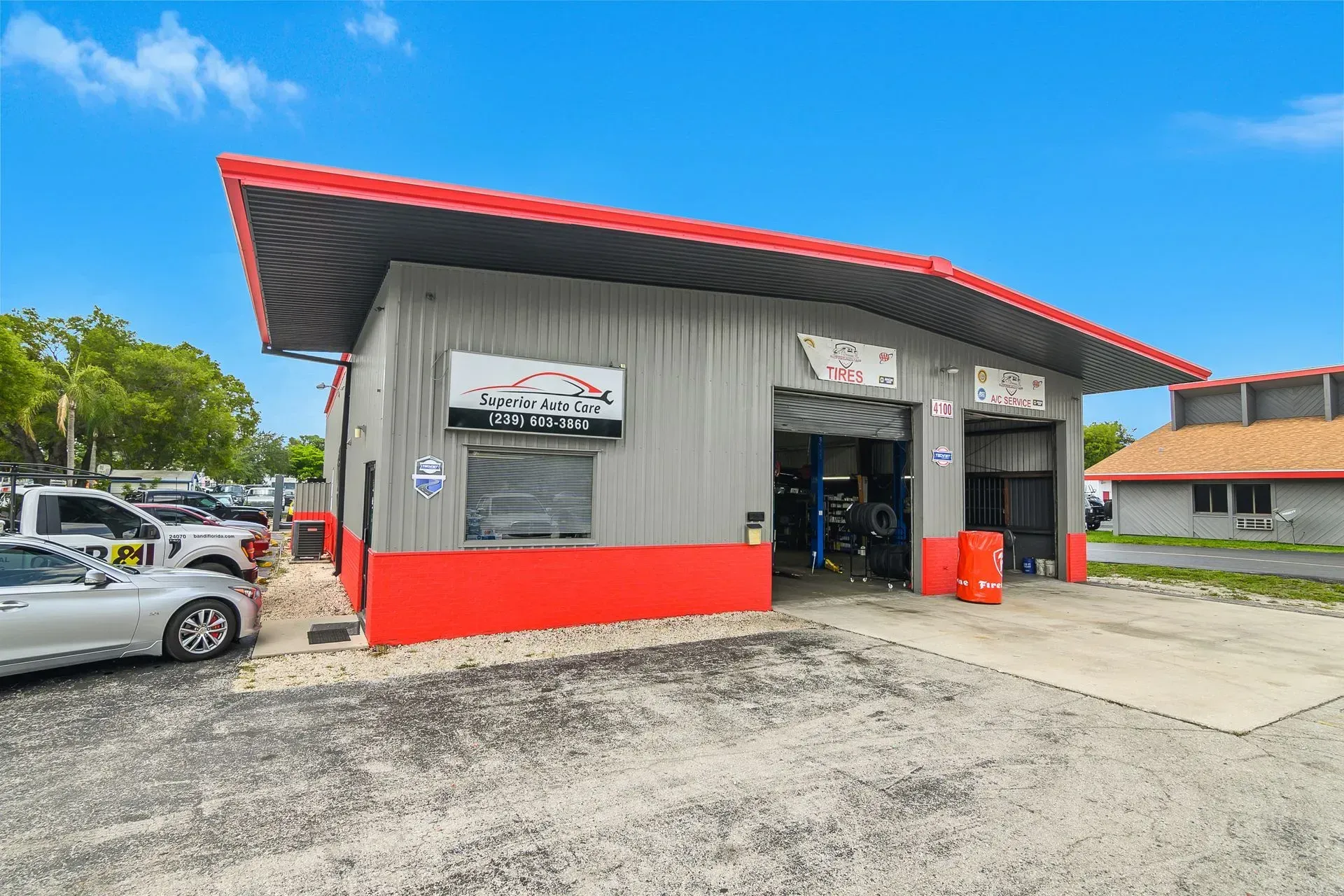 Small gray auto repair shop with red trim and open garage bays on a gravel lot