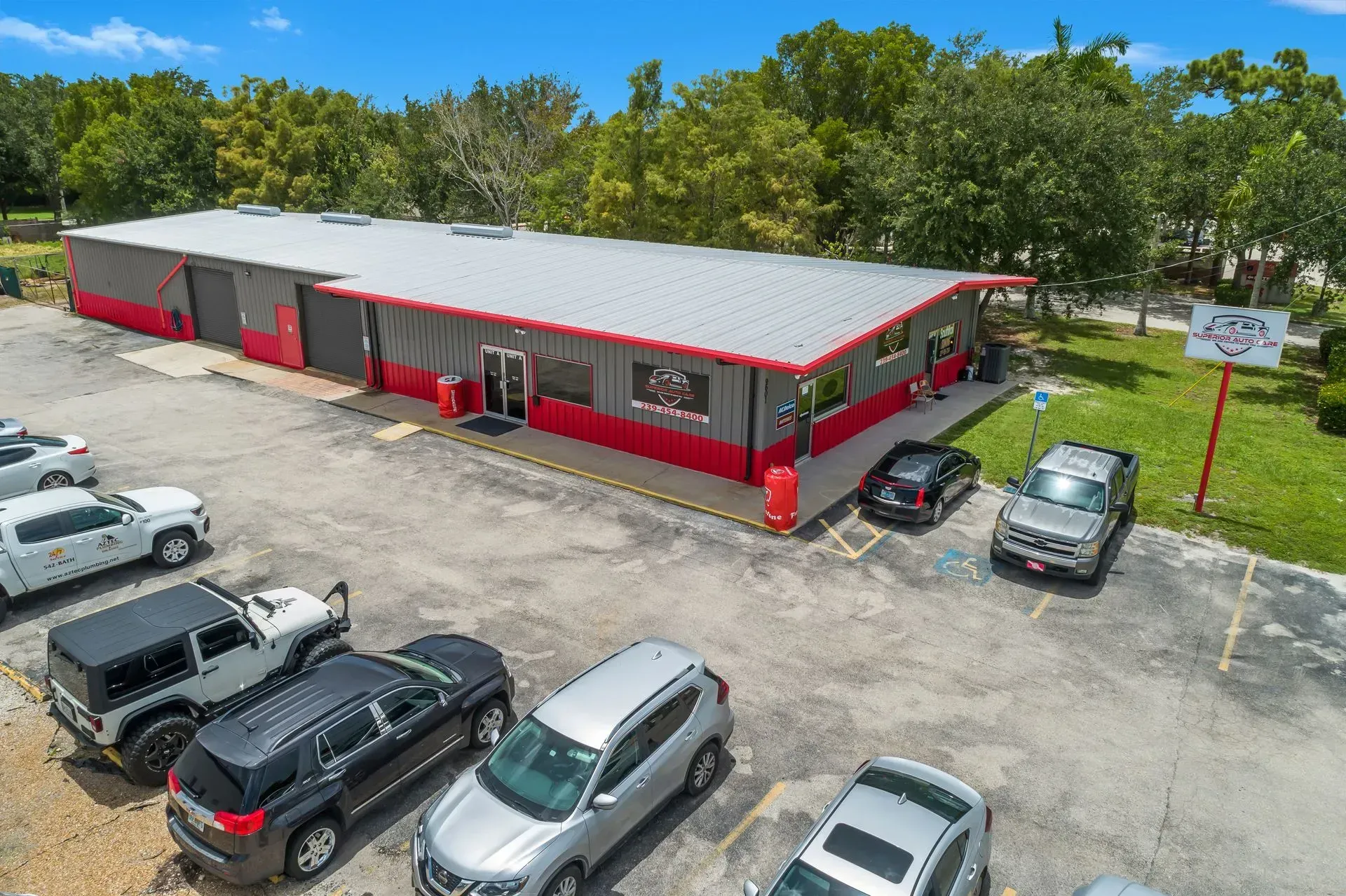 Aerial view of a red commercial building with parked cars and trees around it.