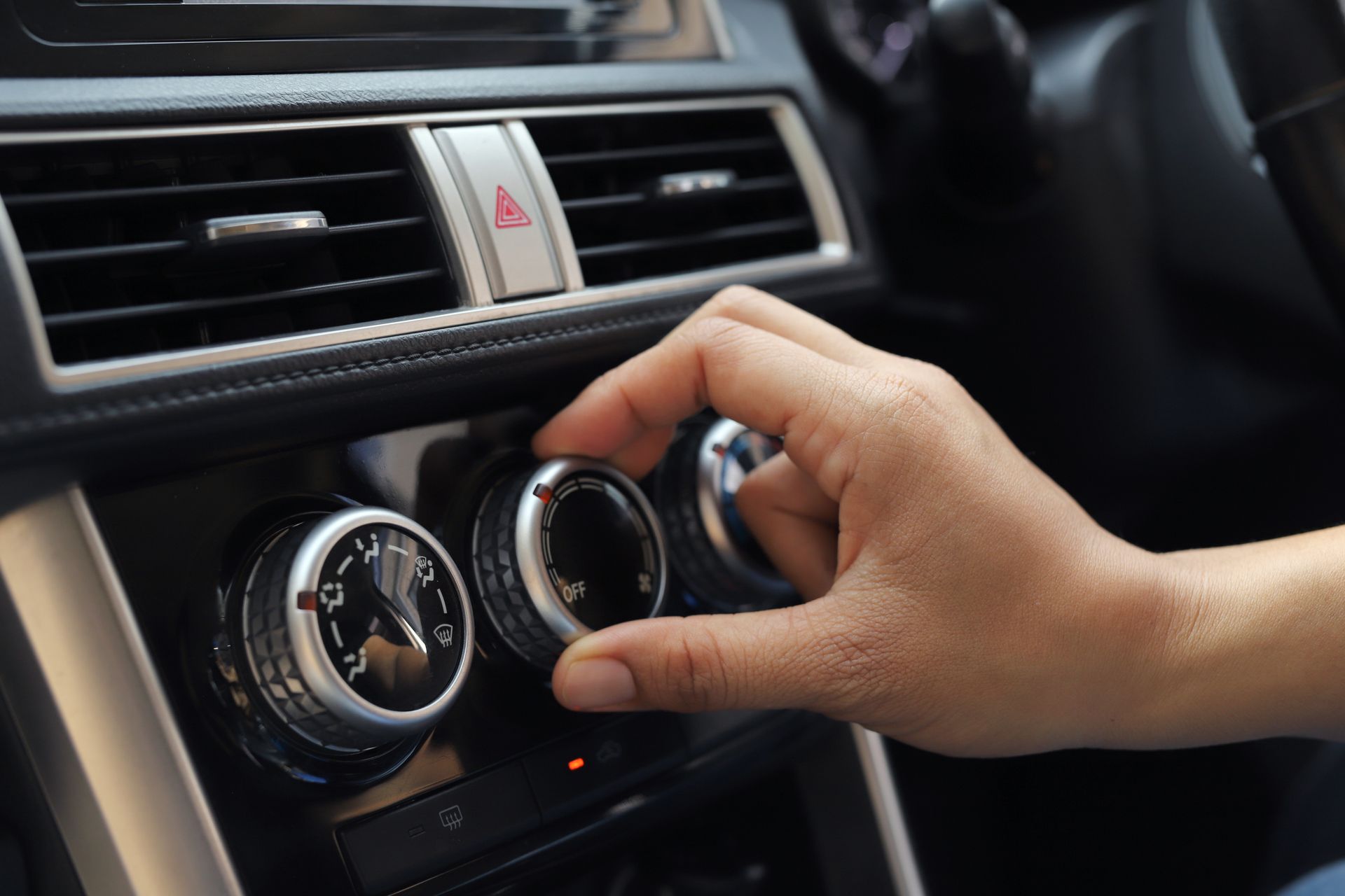 Hand adjusting a car’s climate control knobs on the dashboard