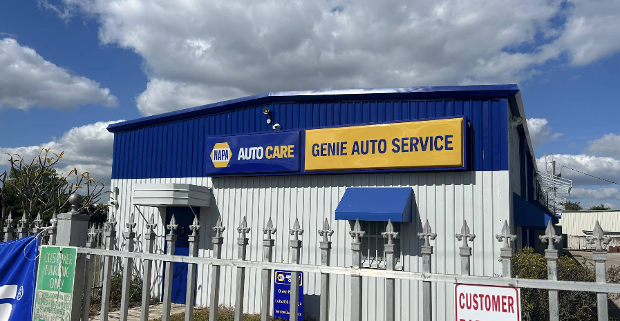 Blue auto service building with white fence, yellow sign, and cloudy sky