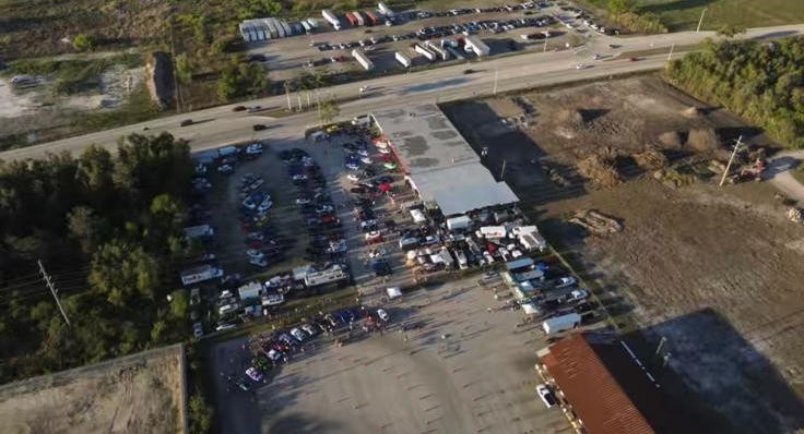Aerial view of a crowded parking lot with many parked cars beside buildings and a road.