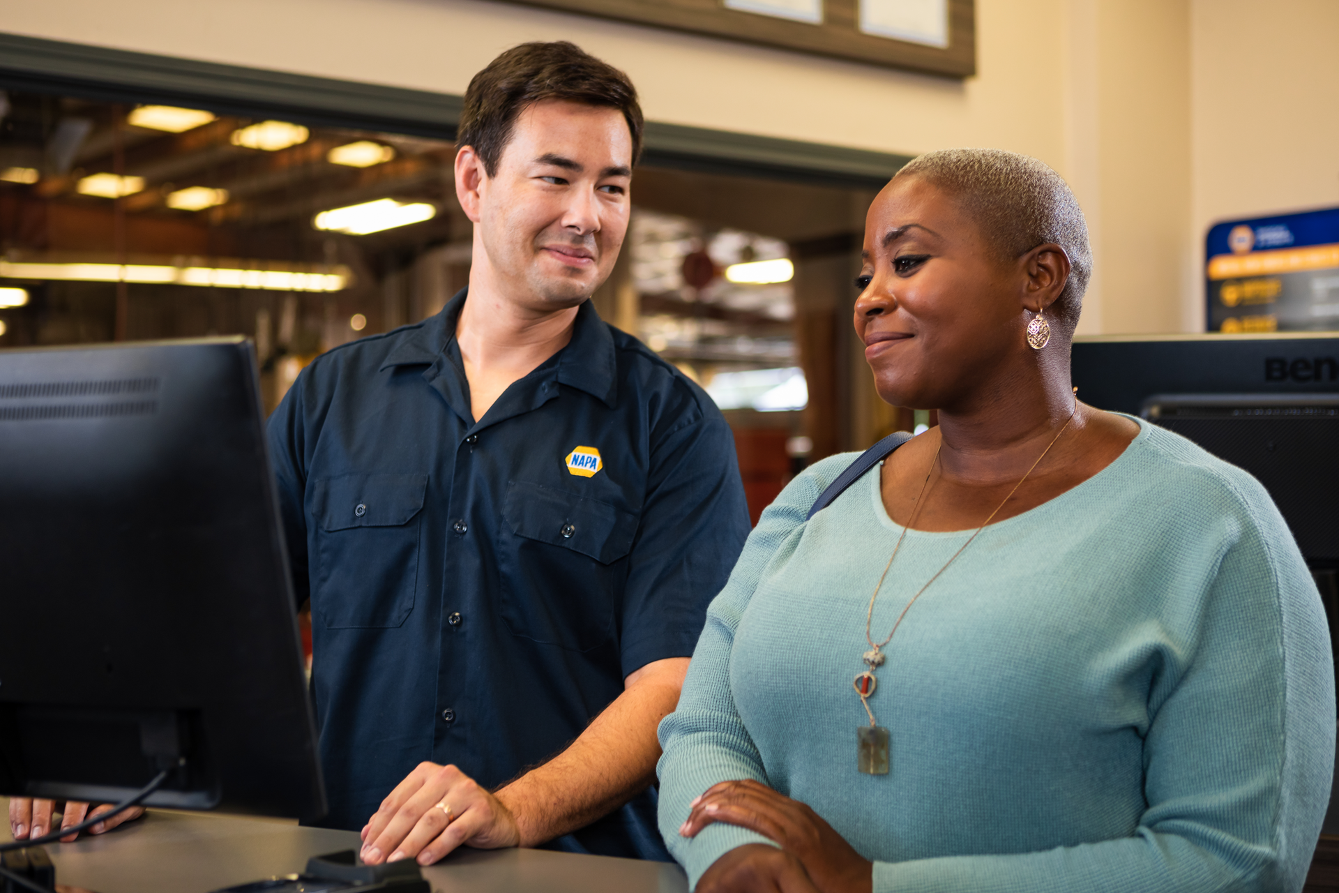 Two coworkers smiling beside computer monitors in a store or office setting