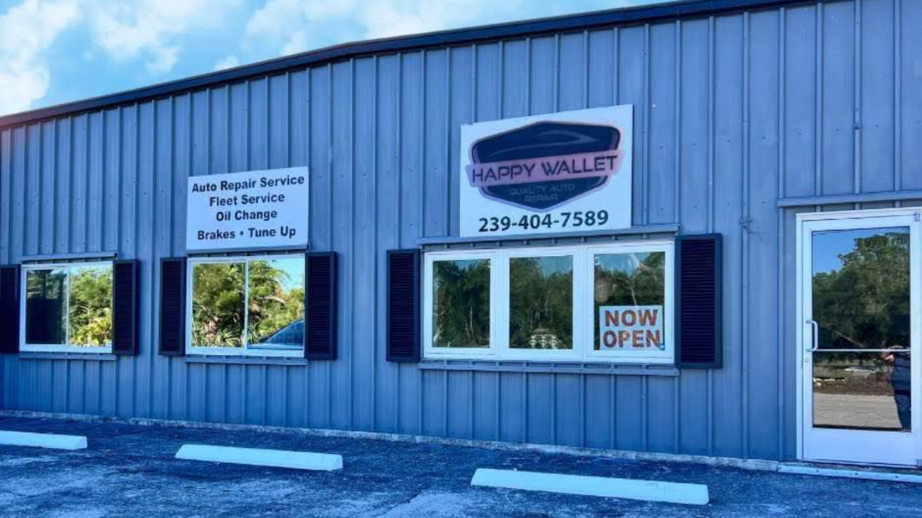 Blue storefront with signs and large windows, including a “Now Open” sign.