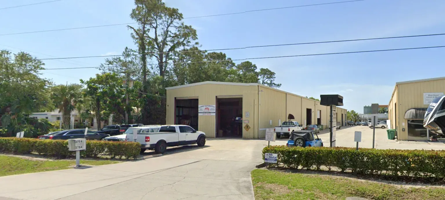 Industrial building with parked cars and a fenced yard on a sunny day
