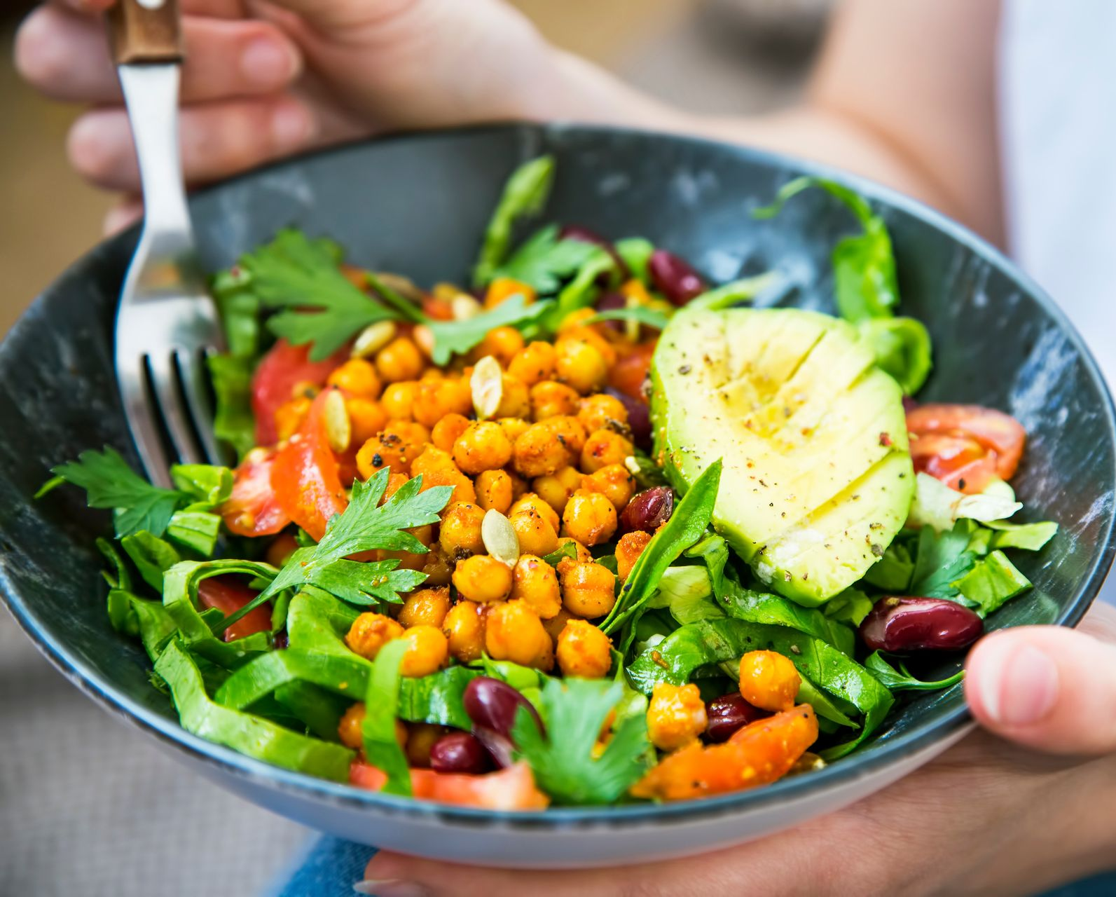 Person holding a bowl of salad with chickpeas, avocado, and tomatoes.