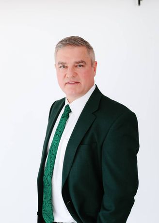 Portrait of Andy Peters Davis in a dark green suit and tie against a white background