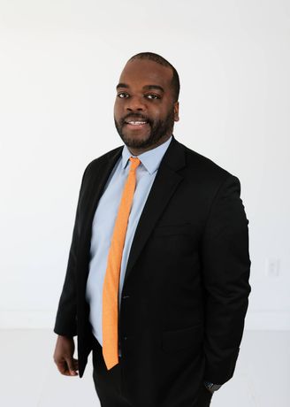 Portrait of Andy Peters Davis in a dark green suit and tie against a white background