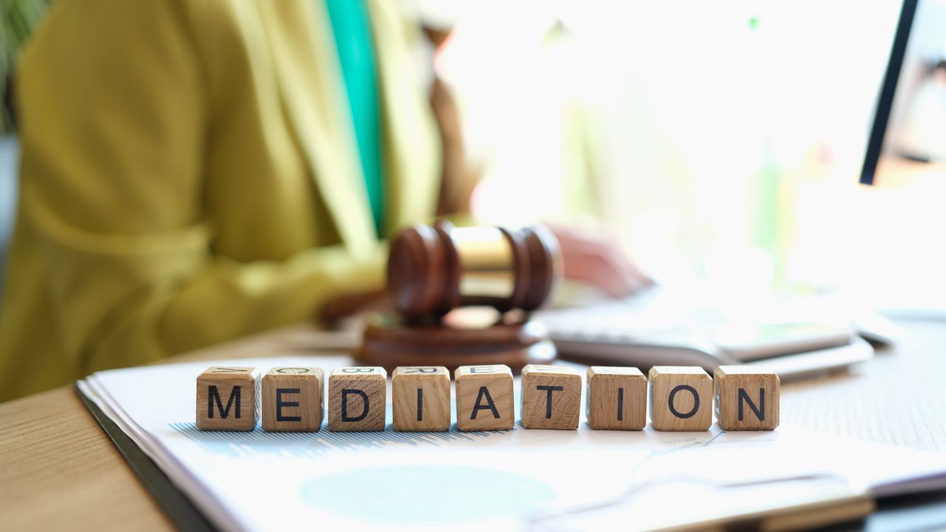 Wooden blocks spelling “MEDIATION” beside a gavel on an open desk document