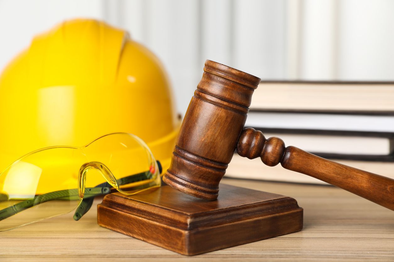 Wooden judge's gavel beside yellow hard hat and safety glasses on a desk