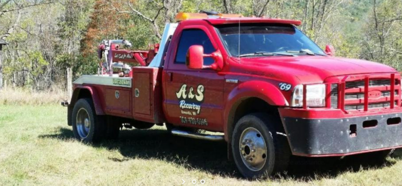 A bright red tow truck with custom lettering parked in a grassy field.