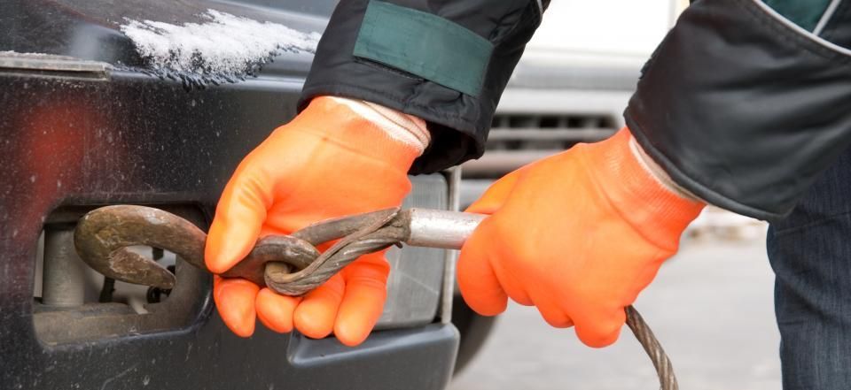 A person wearing bright orange gloves attaches a metal winch hook to a vehicle's towing point.