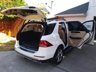 White SUV with rear hatch and right-side doors open in a driveway, showing the cargo area and tan interior