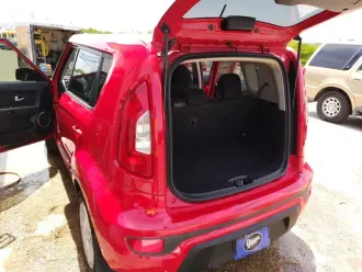 Red hatchback with rear door open, showing empty cargo area in a parking lot.