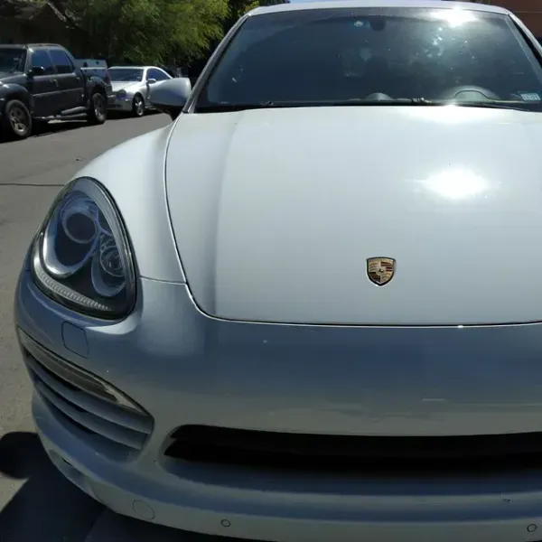 Front view of a silver Porsche sports car parked outdoors on a sunny street.