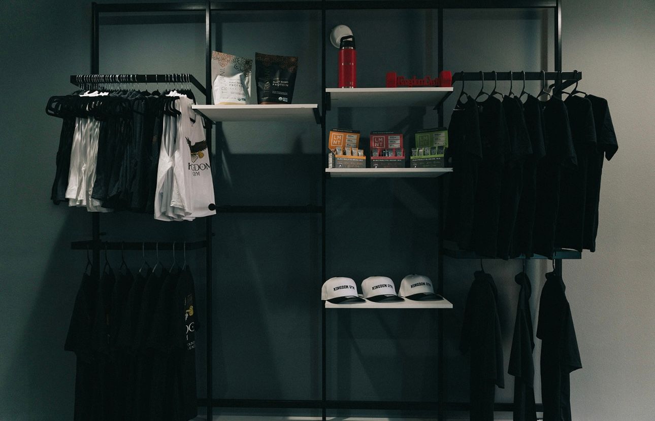 Clothing rack with black shirts, shelves with merchandise, in a store.