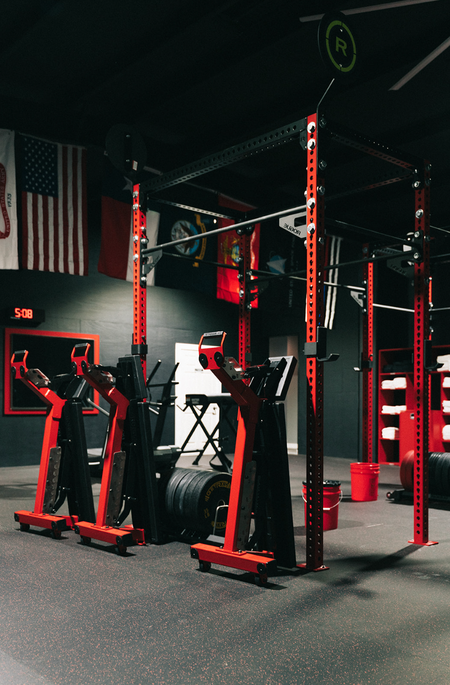 Red squat racks and equipment in a dark gym. Flags hang on the wall.