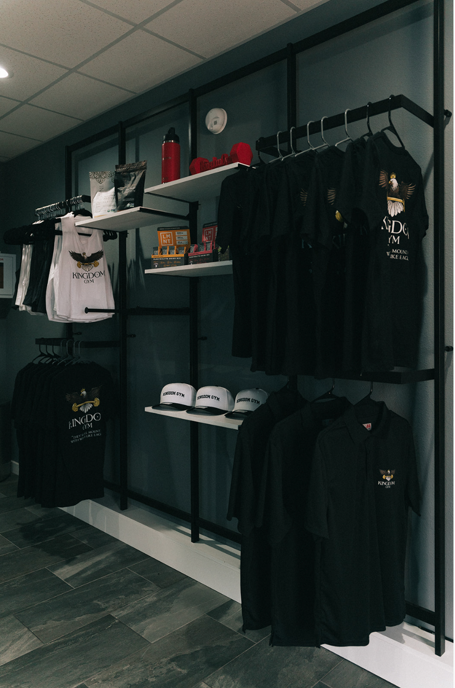 Clothing store display with black tees, hats, and merchandise on shelves and hanging racks.