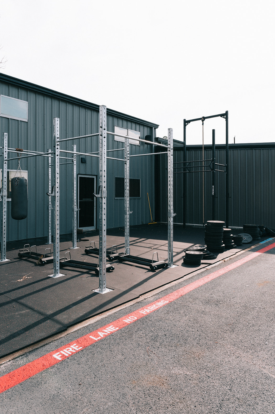 Outdoor gym with pull-up rigs and punching bag near a gray building and asphalt. Red fire lane marking.