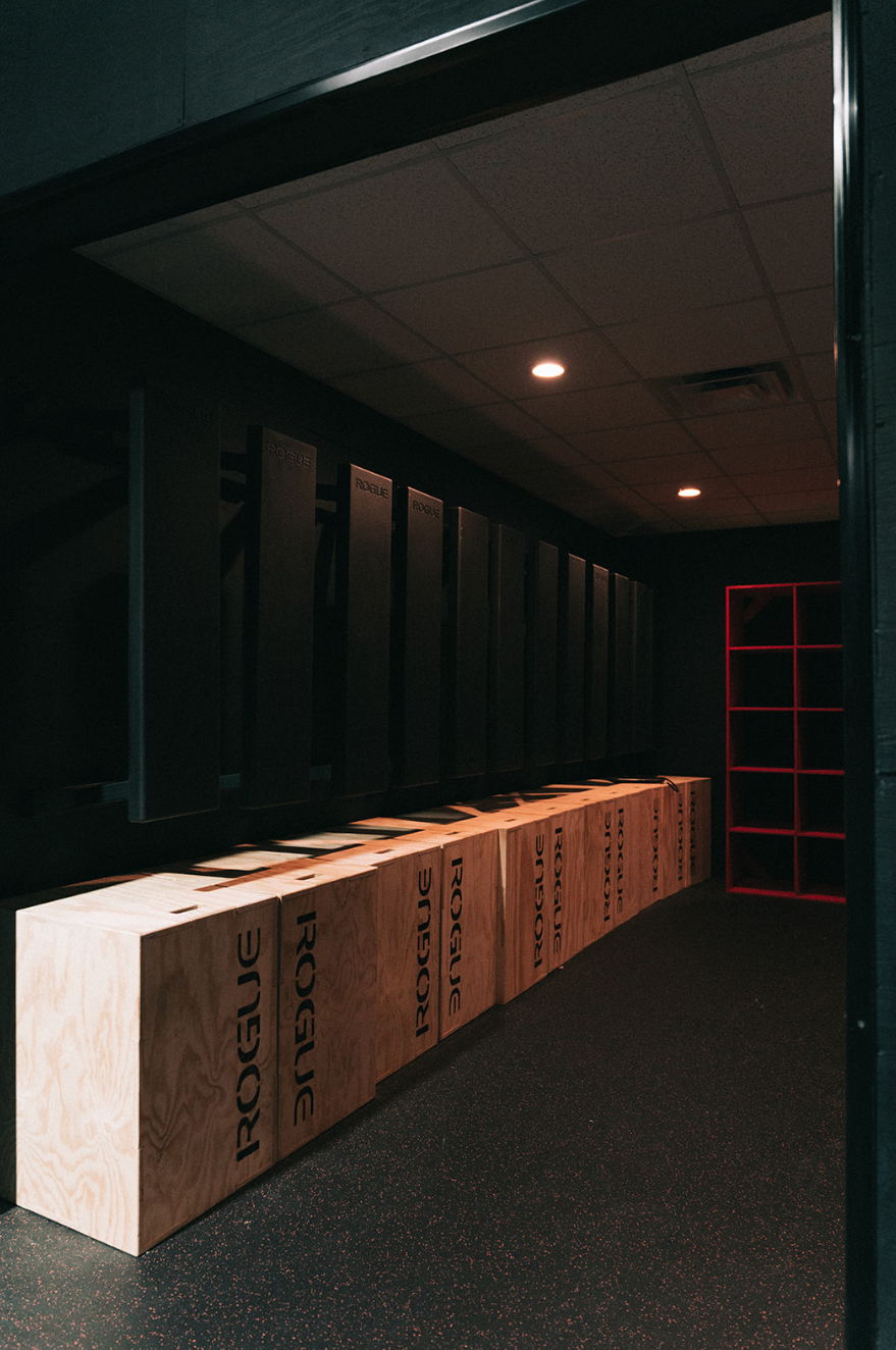 Dark interior of a gym, with wooden boxes, lockers, and a red-framed window.