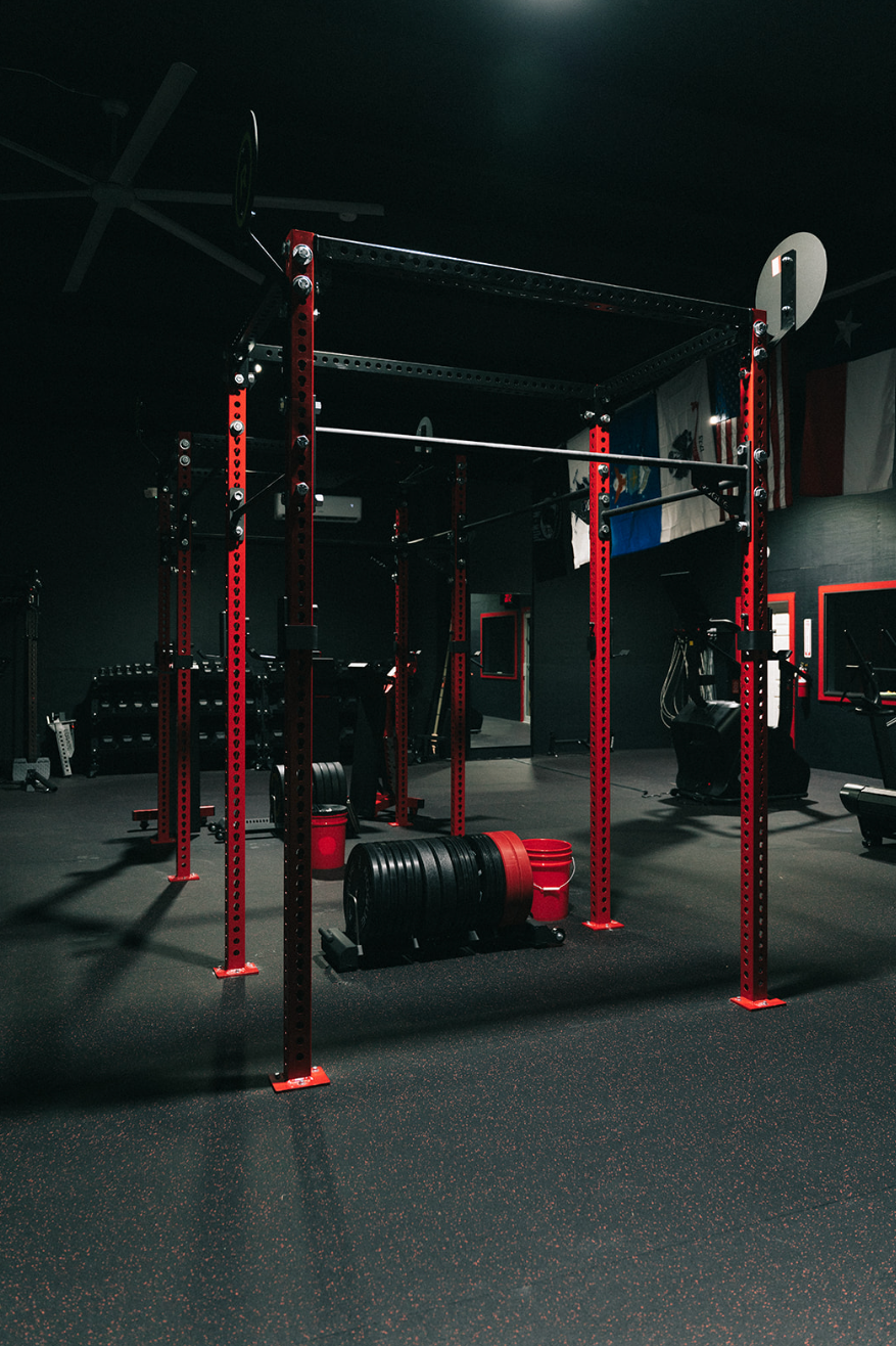 Weightlifting rack in a dark gym with red accents; a barbell is loaded on the rack.