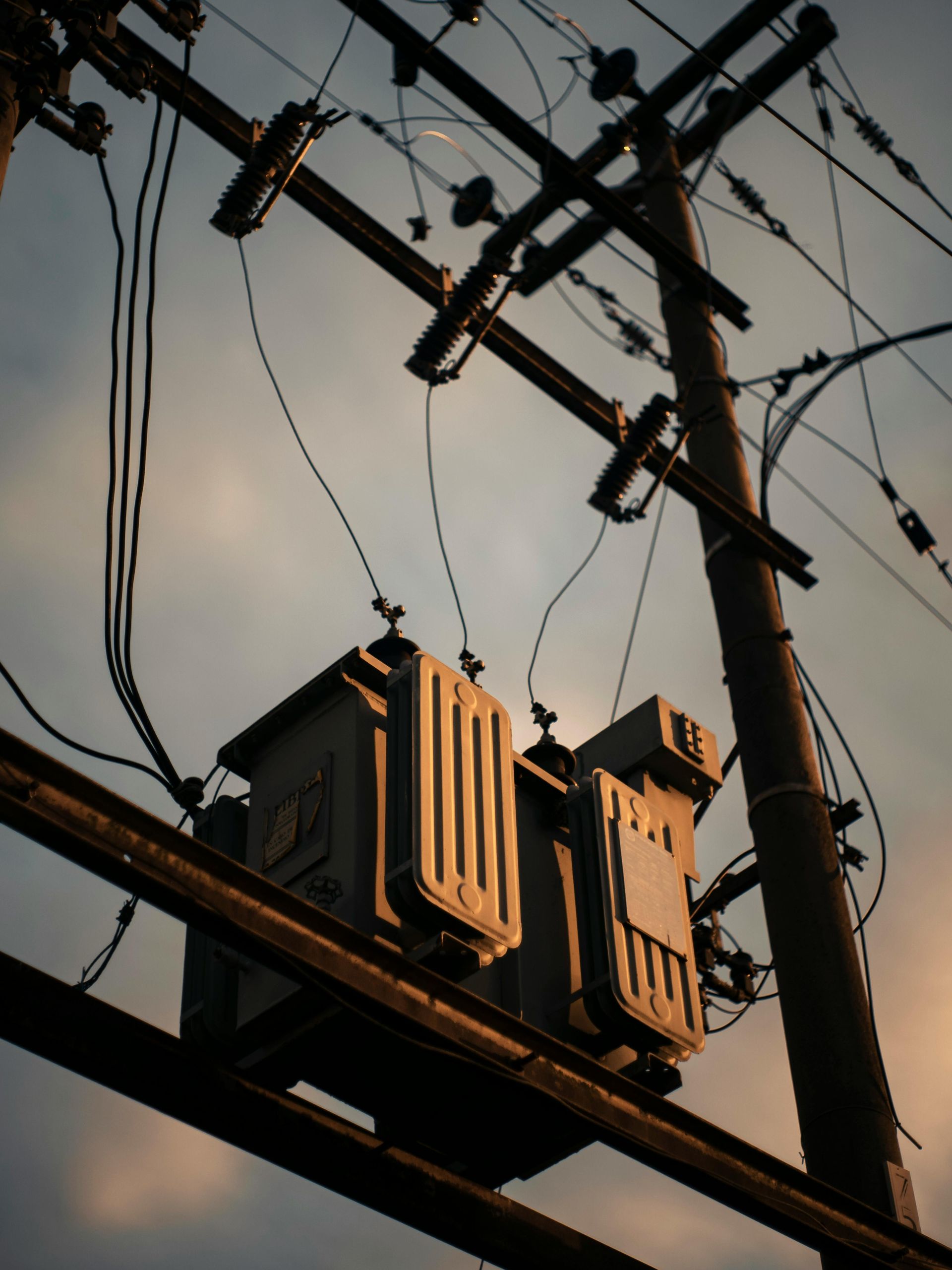 Utility pole with transformers and power lines against a dusk sky