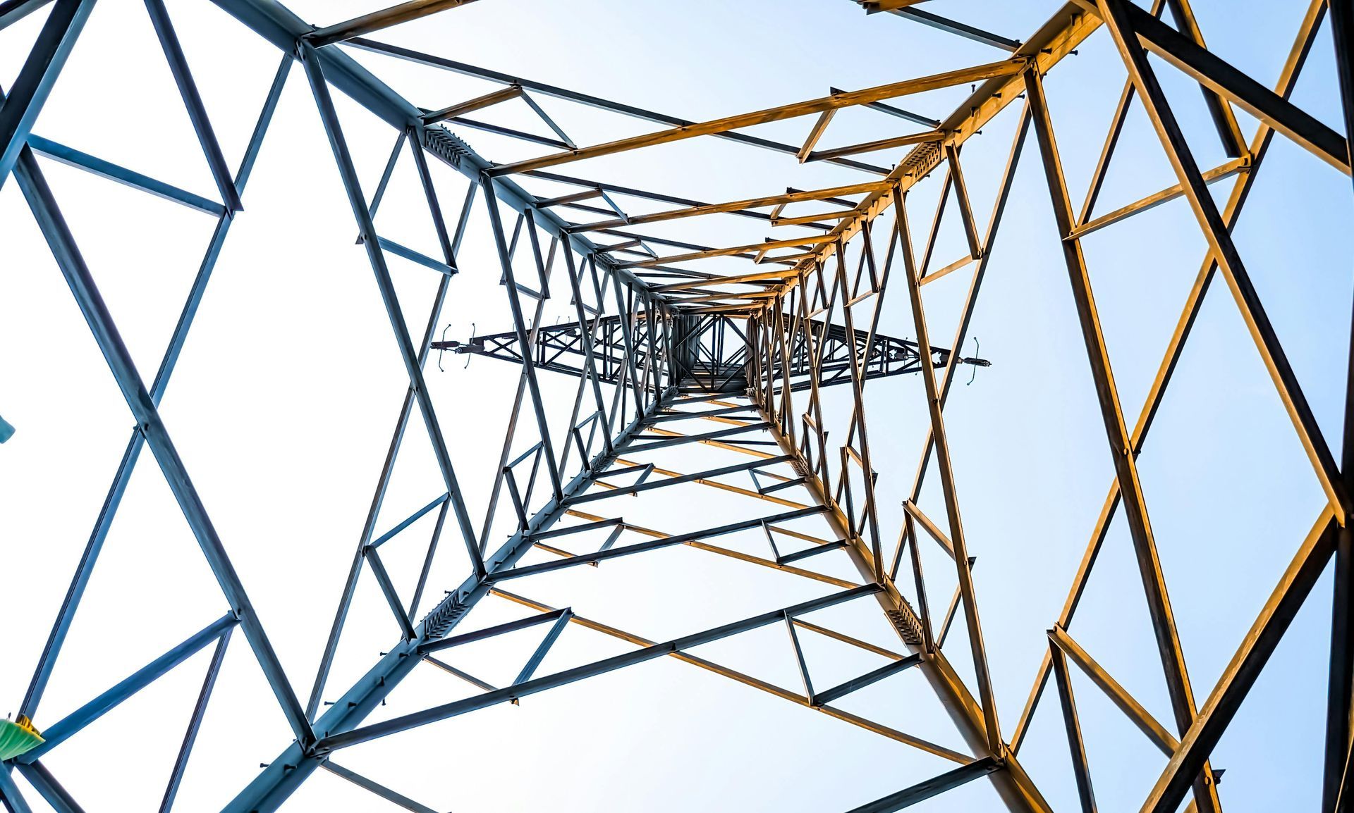 Geometric view looking up through a steel transmission tower with blue and orange framework against the sky