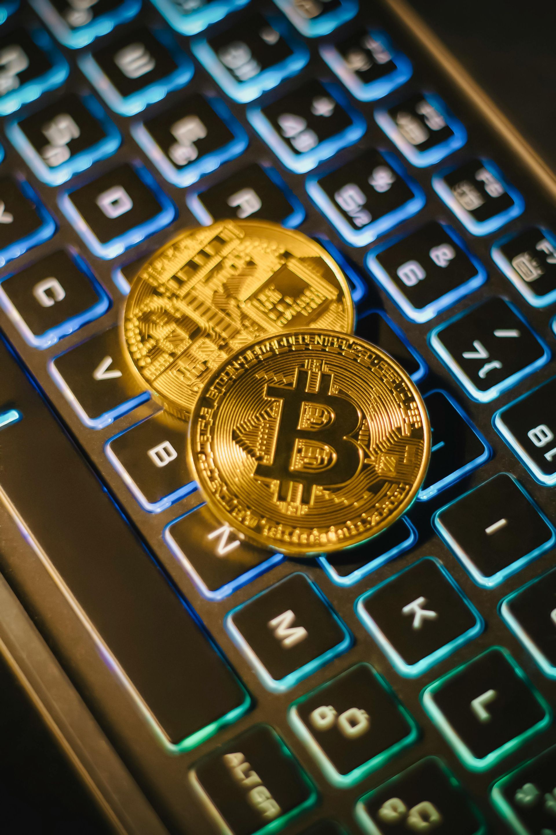 Two gold Bitcoin coins on a backlit keyboard with blue and green keys