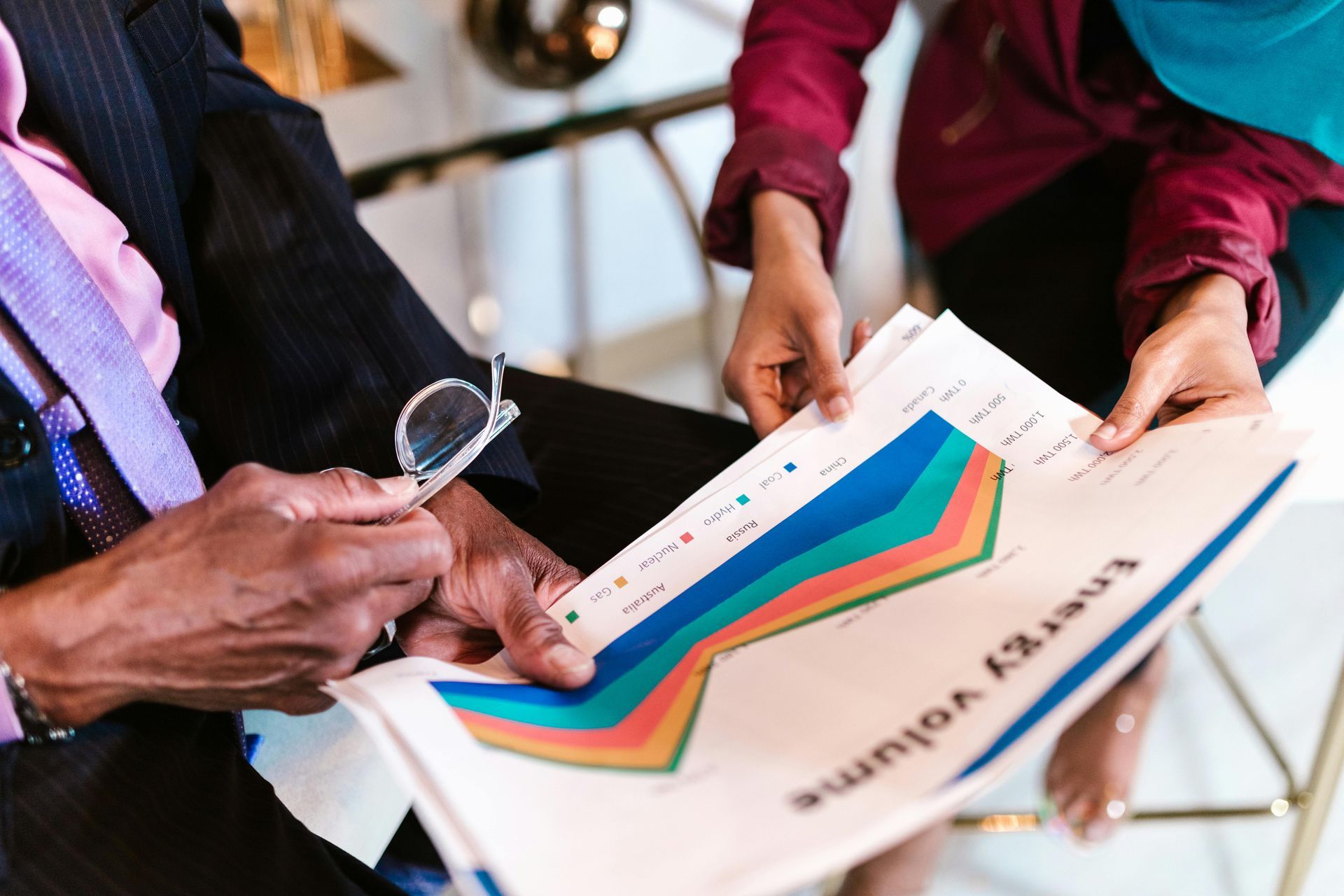 Hands holding a multicolored chart or brochure over a chair in an indoor meeting setting
