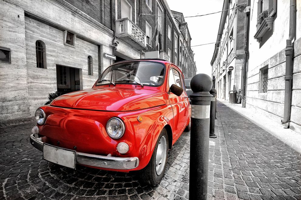 Una macchina rossa è parcheggiata sul lato di una strada acciottolata.