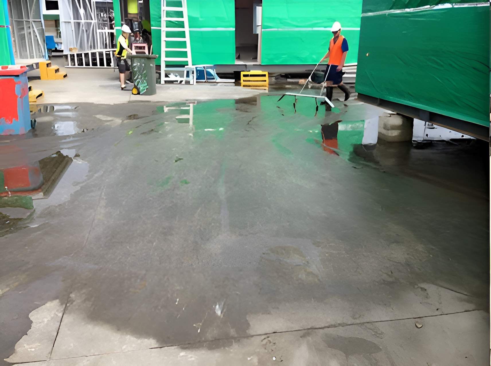 A Man In An Orange Vest Is Walking On A Wet Concrete Floor — EcoPro Pressure Cleaning In Broadbeach Waters, QLD